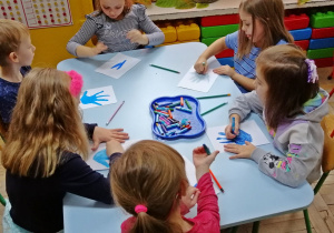 Dzieci kolorują na niebiesko rysunek własnej dłoni